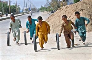 A group of children playing with used motorcycle tyres at Gul Muhammad Khoso Village Road.