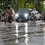 Vehicles pass through stagnant rainwater accumulated at Saddar road after heavy rainfall in the provincial capital