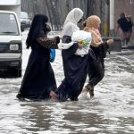Women make their way through a flooded road following heavy monsoon rainfall on Lawrence Road in the provincial capital