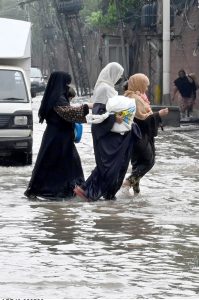 Women make their way through a flooded road following heavy monsoon rainfall on Lawrence Road in the provincial capital