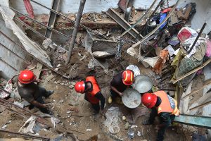 Rescue personnel conduct a search operation amid rubble after the roof of a house collapsed.