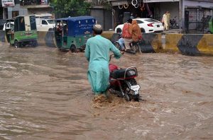 A motorcyclist pushes his motorcycle through floodwater while auto-rickshaws navigate a submerged road in the Budni area following heavy monsoon rains in the provincial capital.