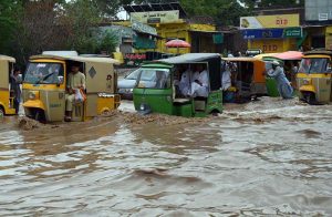 A motorcyclist pushes his motorcycle through floodwater while auto-rickshaws navigate a submerged road in the Budni area following heavy monsoon rains in the provincial capital.