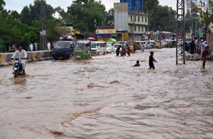 A motorcyclist pushes his motorcycle through floodwater while auto-rickshaws navigate a submerged road in the Budni area following heavy monsoon rains in the provincial capital.