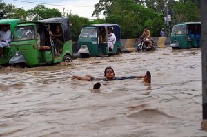 A motorcyclist pushes his motorcycle through floodwater while auto-rickshaws navigate a submerged road in the Budni area following heavy monsoon rains in the provincial capital.