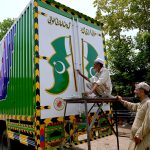 Truck art painter busy in giving final touches to a Pakistani flag on a delivery truck at his workplace on Ring road