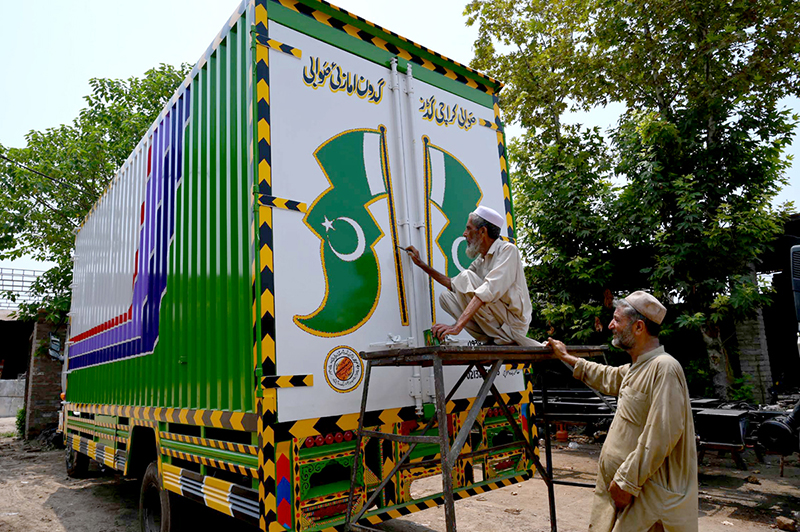 Truck art painter busy in giving final touches to a Pakistani flag on a delivery truck at his workplace on Ring road