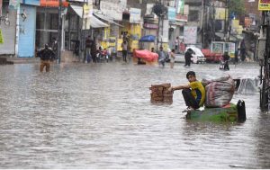 Commuters wade through a flooded road following heavy monsoon rain in the city, causing severe disruption to traffic and daily life.