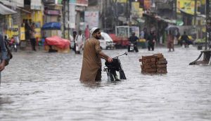Commuters wade through a flooded road following heavy monsoon rain in the city, causing severe disruption to traffic and daily life.