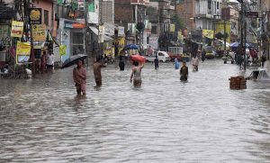 Commuters wade through a flooded road following heavy monsoon rain in the city, causing severe disruption to traffic and daily life.