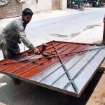 A man is painting an iron gate on the side of the road at his workshop