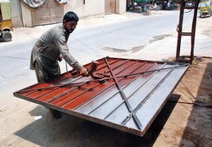 A man is painting an iron gate on the side of the road at his workshop