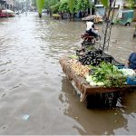 A vegetable vendor waits for customers while sitting on a chair amid rainwater accumulated on the roadside after heavy rainfall in the Provincial Capital