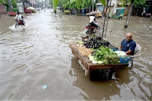 A vegetable vendor waits for customers while sitting on a chair amid rainwater accumulated on the roadside after heavy rainfall in the Provincial Capital