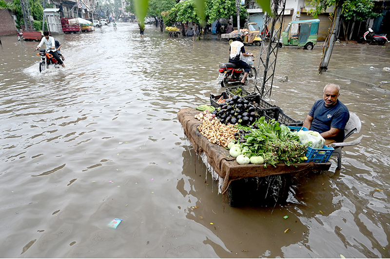 A vegetable vendor waits for customers while sitting on a chair amid rainwater accumulated on the roadside after heavy rainfall in the Provincial Capital