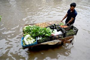 A vegetable vendor waits for customers while sitting on a chair amid rainwater accumulated on the roadside after heavy rainfall in the Provincial Capital