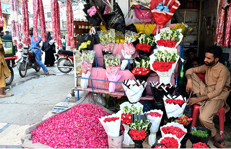 A vendor arranges and displays colourful flower bouquets garlands and flower petals to attract customers at Banni Chowk