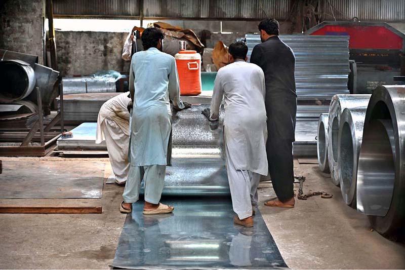 Workers are manually unrolling a heavy steel coil to make door frames (chokhat) in a warehouse on City Saddar Road