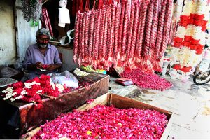 A vendor arranges and displays colourful flower bouquets garlands and flower petals to attract customers at Banni Chowk