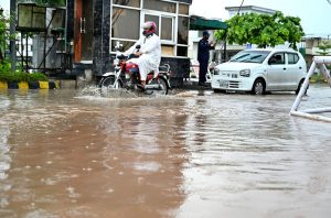 A motorcyclist and vehicle passing through rain water accumulated on road at the entrance of Media Town after rain in the city.