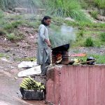 A vendor is busy roasting corn cobs for customers at his roadside setup