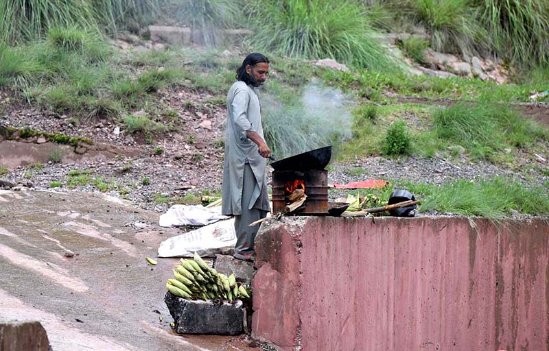 A vendor is busy roasting corn cobs for customers at his roadside setup