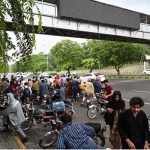 Motorcyclists take shelter under a bus stop shed along Islamabad Expressway to protect them from heavy rain