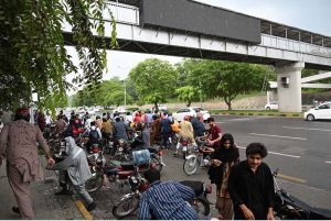 Motorcyclists take shelter under a bus stop shed along Islamabad Expressway to protect them from heavy rain