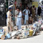 Labourers, carrying their tools, sit along the roadside waiting for clients to hire them for work at Banni Chowk