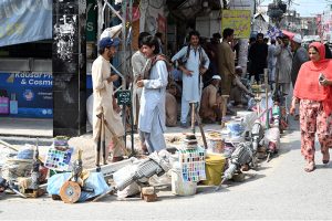 Labourers, carrying their tools, sit along the roadside waiting for clients to hire them for work at Banni Chowk