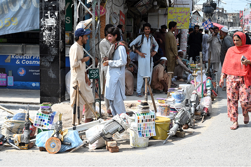 Labourers, carrying their tools, sit along the roadside waiting for clients to hire them for work at Banni Chowk