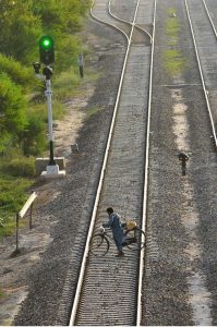 A cyclist risks his life while pushing his bicycle across the main railway track beside an illuminated green signal at Piran Ghaib Railway Station, despite the indication of an approaching train.