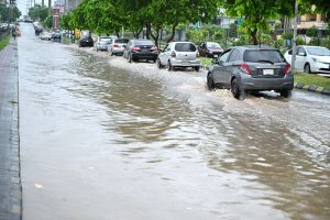 A motorcyclist and vehicle passing through rain water accumulated on road at the entrance of Media Town after rain in the city.