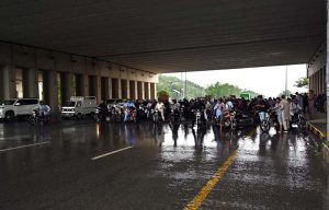 Motorcyclists take shelter under a bus stop shed along Islamabad Expressway to protect them from heavy rain