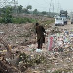 A young boy searches for recyclable items amid piles of garbage strewn along the roadside