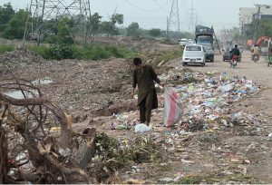 A young boy searches for recyclable items amid piles of garbage strewn along the roadside