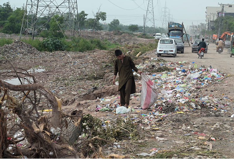 A young boy searches for recyclable items amid piles of garbage strewn along the roadside