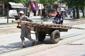 An elderly man pulls a handcart loaded with bamboo poles through a street