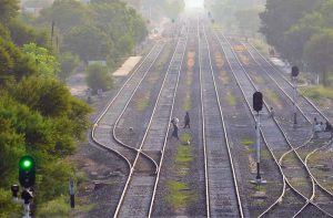 A cyclist risks his life while pushing his bicycle across the main railway track beside an illuminated green signal at Piran Ghaib Railway Station, despite the indication of an approaching train.