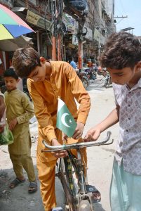 A boy is putting a Pakistani flag on a bicycle in connection with the upcoming Independence Day celebrations.