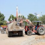 Workers load crushed stones into a tractor trolley during ongoing road rehabilitation work in the city