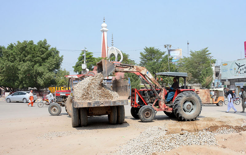 Workers load crushed stones into a tractor trolley during ongoing road rehabilitation work in the city