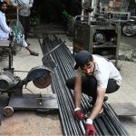 A worker measures and cuts steel pipes at a metal workshop