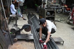 A worker measures and cuts steel pipes at a metal workshop
