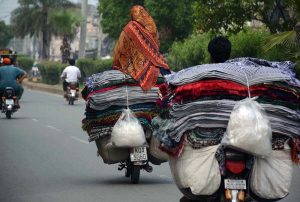 An elderly street vendor carries inflatable handballs while strolling through a street in search of customers