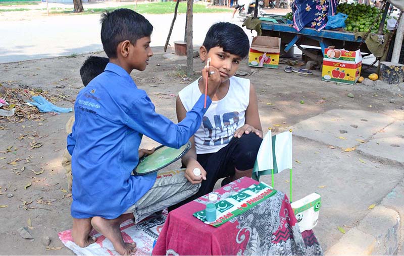 A youngster paints the face of a boy with the colors of the national flag in connection with the upcoming Independence Day celebrations
