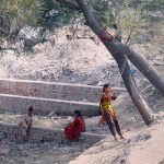 A makeshift swing hangs from a tree as girls enjoy a moment of recreation at a roadside site amid piles of construction debris in the city
