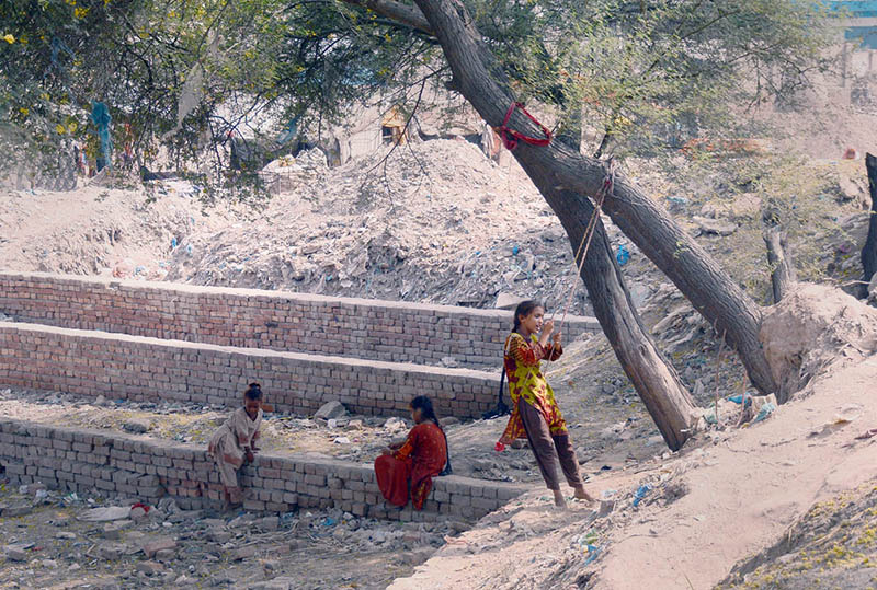 A makeshift swing hangs from a tree as girls enjoy a moment of recreation at a roadside site amid piles of construction debris in the city