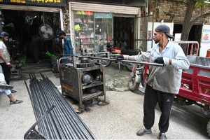 A worker measures and cuts steel pipes at a metal workshop