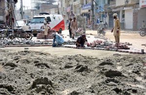 Labourers are busy fixing cemented tiles during repairing work on Main Hussain Agahi Road.